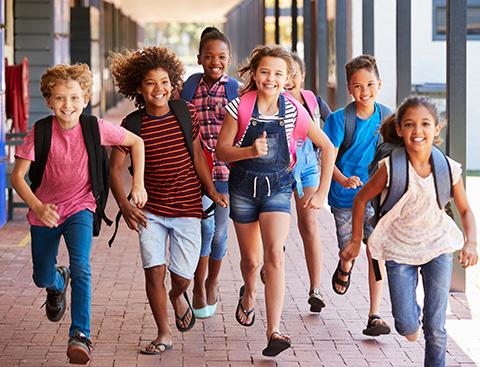 A diverse group of young students runs through a school hallway.